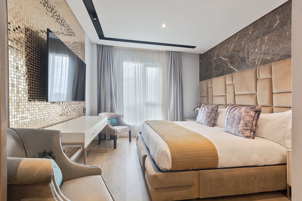 Modern bedroom featuring a luxurious upholstered headboard, marble feature wall, gold mosaic accent wall, and high-quality timber flooring with recessed ceiling lighting.