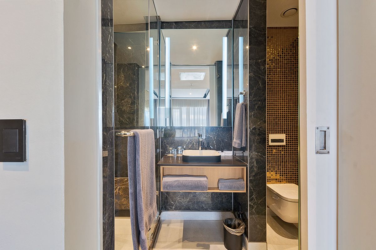 Modern bathroom featuring dark marble wall cladding, a sleek vessel sink with wall-mounted faucet, LED mirror, and a separate toilet area with mosaic tiles.