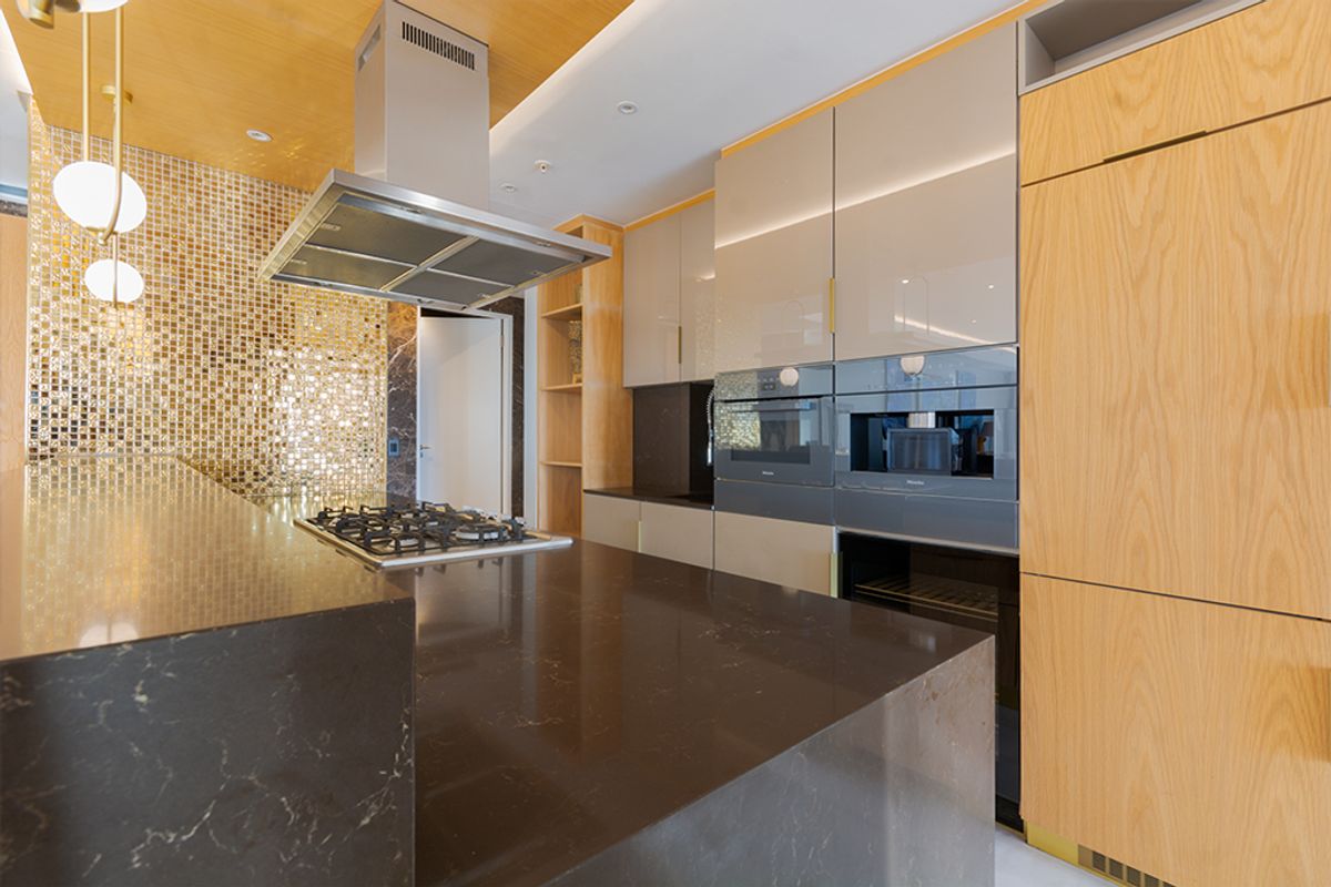 Modern kitchen featuring high-end integrated appliances, stone countertops, a gas hob, and a striking gold mosaic tile backsplash with warm wood cabinetry.