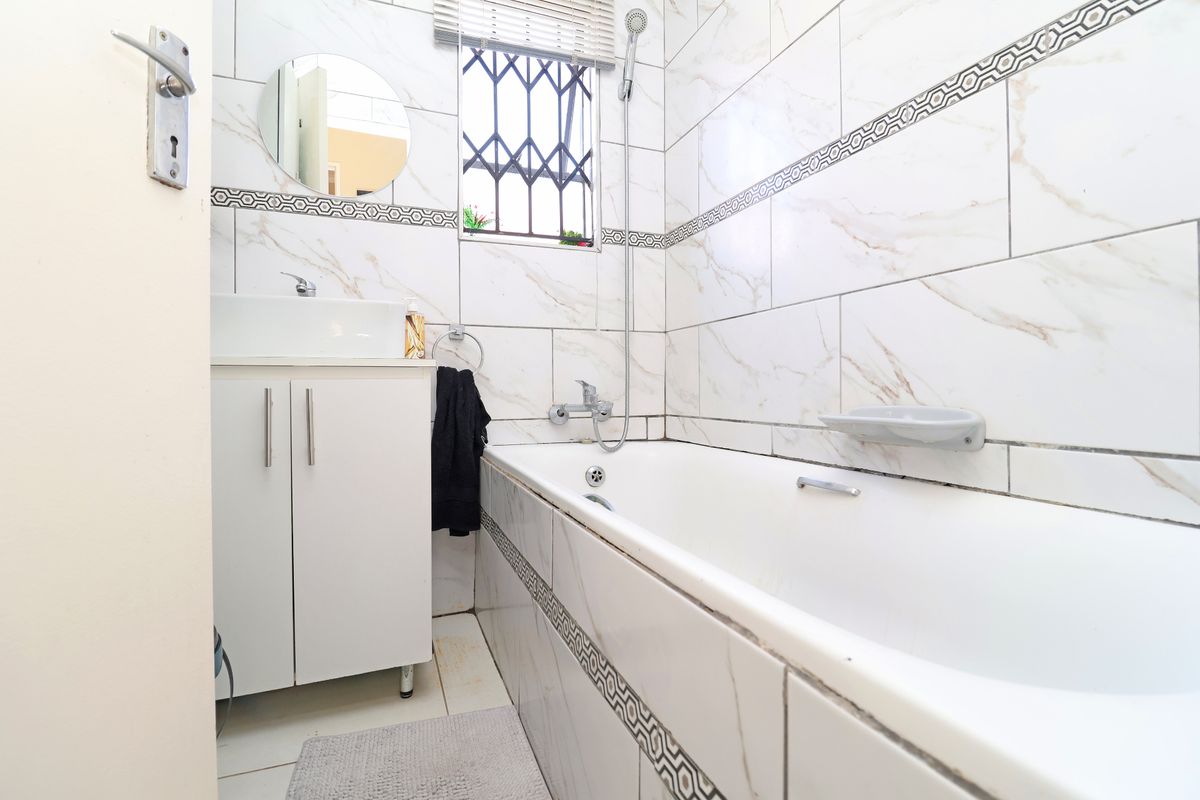 A clean, modern bathroom featuring white marble-look wall tiles, a built-in vanity with basin, and a bathtub with integrated shower fixtures.
