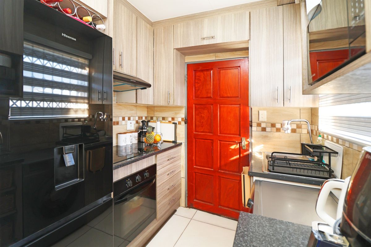 Compact kitchen featuring modern wood-look cabinetry, granite countertops, built-in oven, hob, extractor fan, and a tiled backsplash.