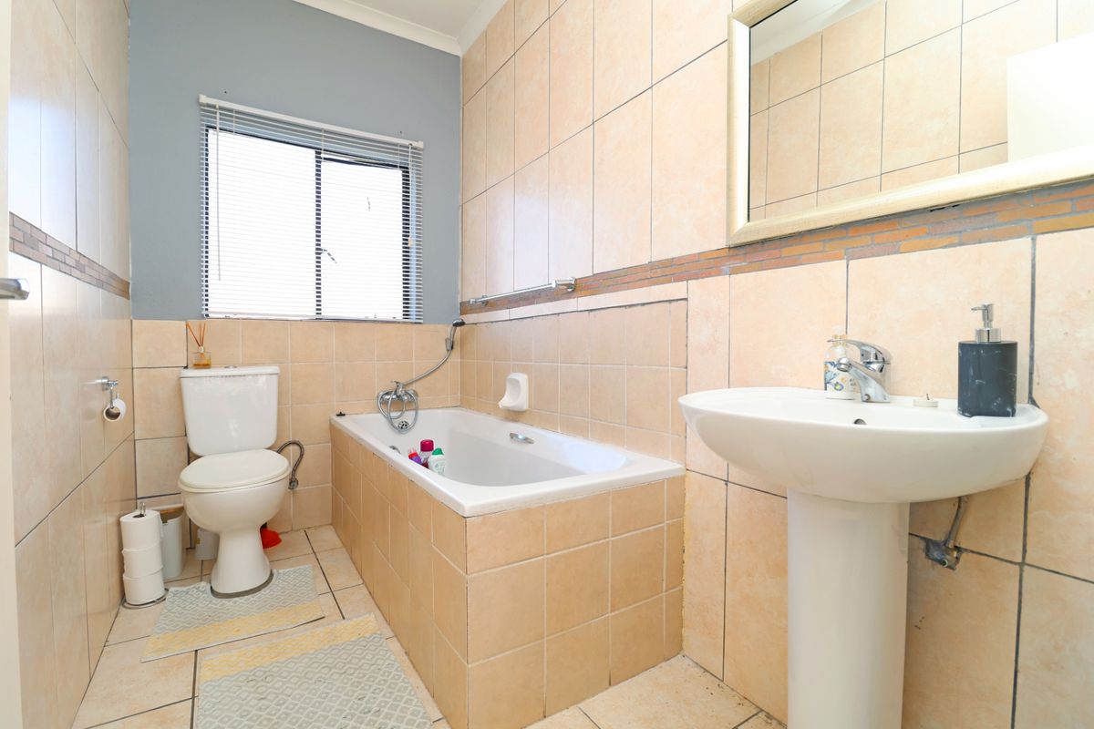A functional bathroom featuring a pedestal basin, built-in bathtub with shower attachment, and tiled finishes throughout.