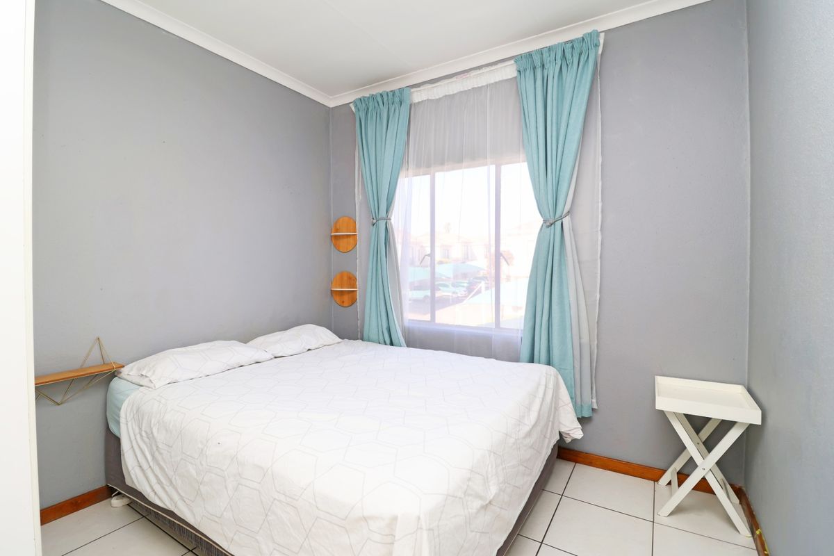 A bedroom featuring tiled flooring, neutral grey walls, and a window with curtains, providing a functional and well-lit sleeping space.