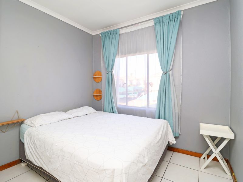 A bedroom featuring tiled flooring, neutral grey walls, and a window with curtains, providing a functional and well-lit sleeping space.
