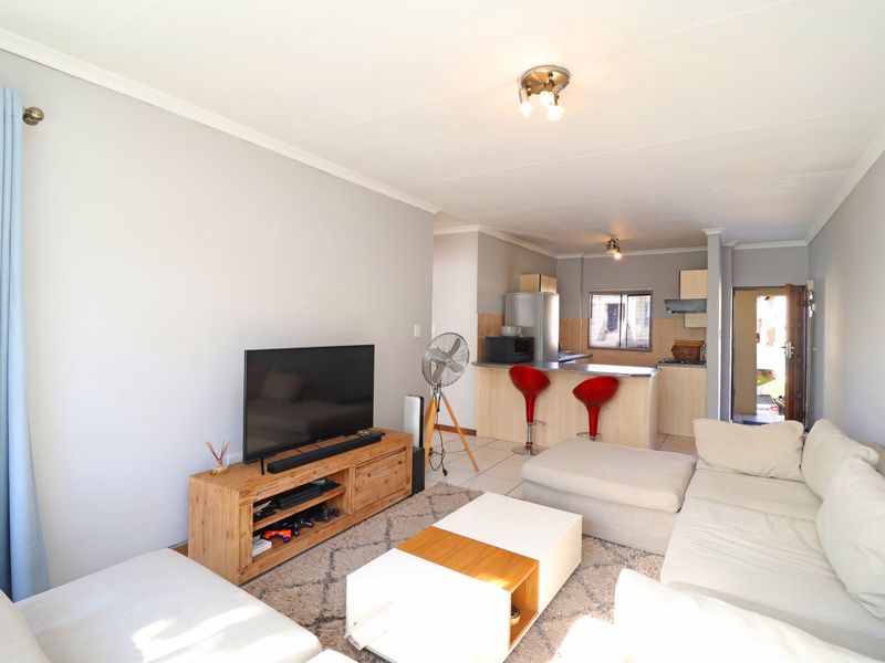 Open-plan living area featuring a combined lounge and kitchen space with a breakfast bar, tiled flooring, and neutral wall finishes.