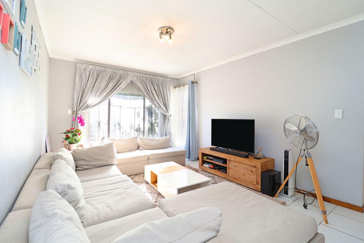 A bright and functional living room featuring tiled flooring and large windows with curtain rails, offering a comfortable and well-lit living space.