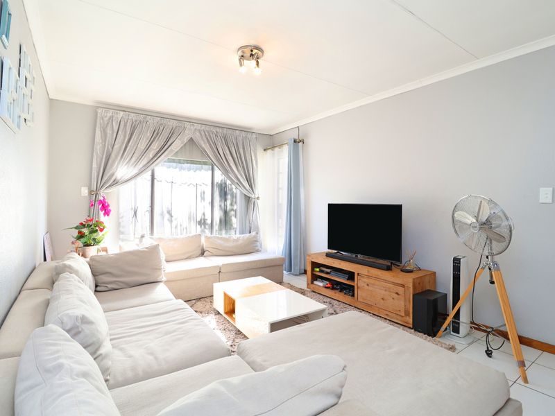 A bright and functional living room featuring tiled flooring and large windows with curtain rails, offering a comfortable and well-lit living space.