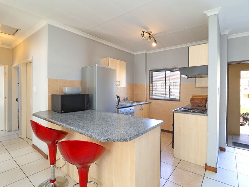 A functional kitchen featuring light wood-finish cabinetry, a breakfast bar, tiled splashbacks, and ceramic floor tiles, offering a practical layout for daily use.