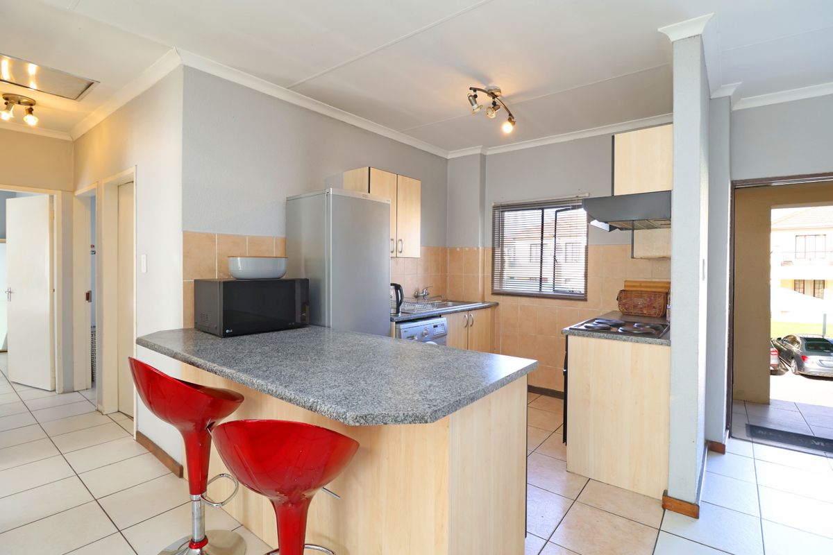 A functional kitchen featuring light wood-finish cabinetry, a breakfast bar, tiled splashbacks, and ceramic floor tiles, offering a practical layout for daily use.