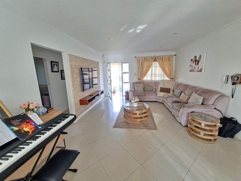 Spacious living room featuring large format floor tiles, a textured stone feature wall, and direct access to the exterior through a security gate.