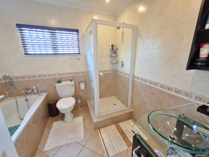 A functional bathroom featuring a built-in bathtub, separate shower enclosure, toilet, and a modern glass vessel sink with tiled finishes throughout.