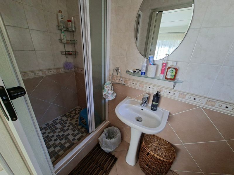 A functional bathroom featuring a pedestal basin, shower enclosure with glass door, and neutral wall and floor tiling.
