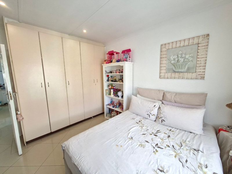 A well-lit bedroom featuring neutral tiled flooring and extensive built-in cupboard storage, providing a functional and clean living space.