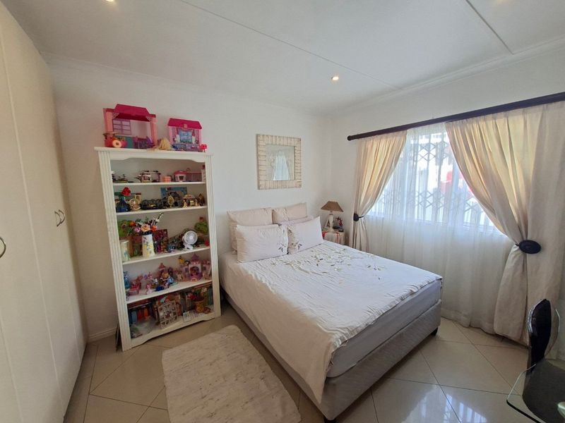 A well-lit bedroom featuring tiled flooring, a built-in wardrobe, and a security gate on the window, providing a functional and comfortable living space.