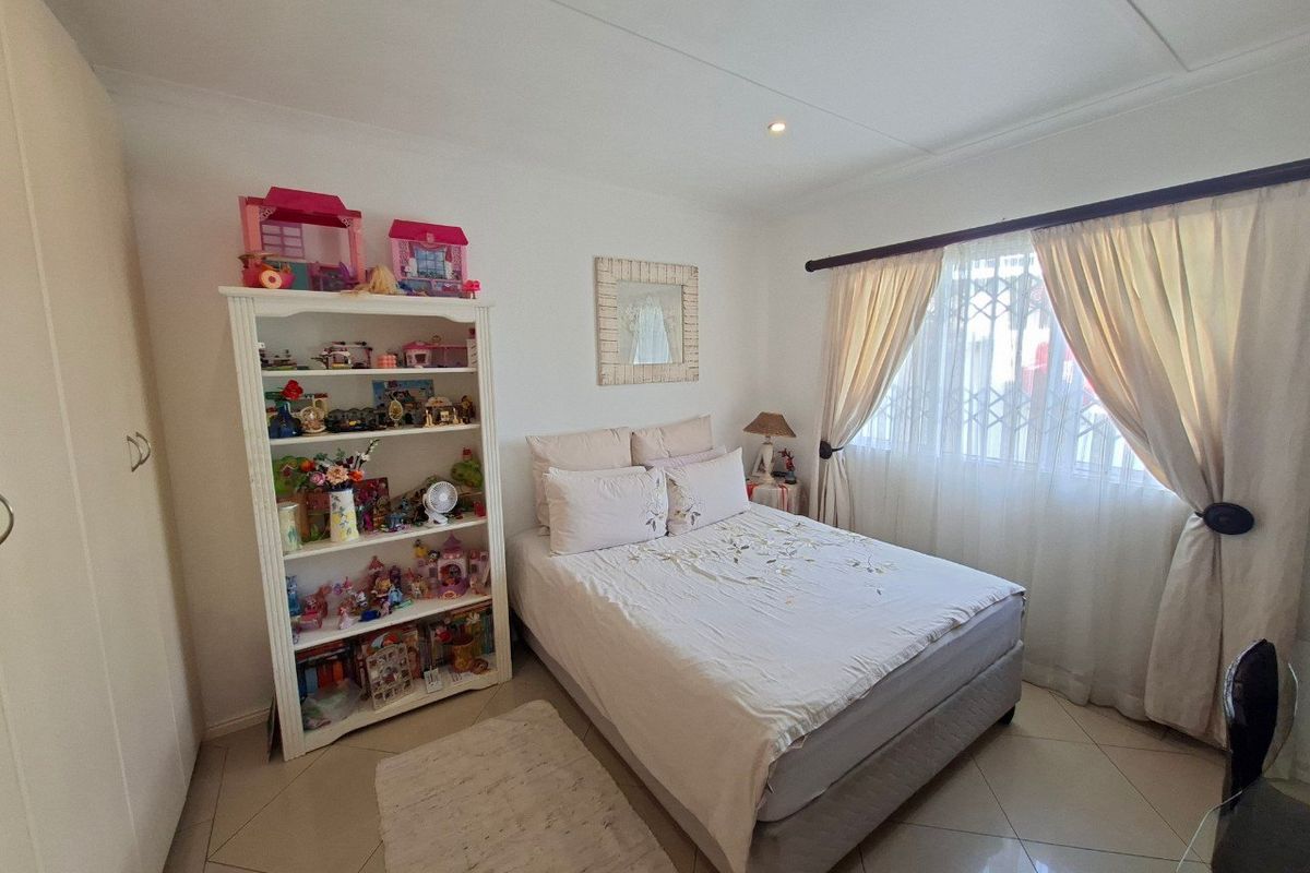A well-lit bedroom featuring tiled flooring, a built-in wardrobe, and a security gate on the window, providing a functional and comfortable living space.