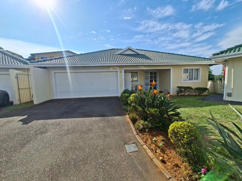 Front elevation of a townhouse featuring a tiled roof, double garage, paved driveway, and a well-maintained front garden with security features.