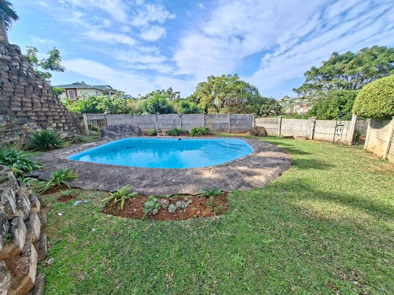 Outdoor pool area featuring a swimming pool with stone coping, surrounded by a lawn and enclosed by a precast concrete boundary wall.