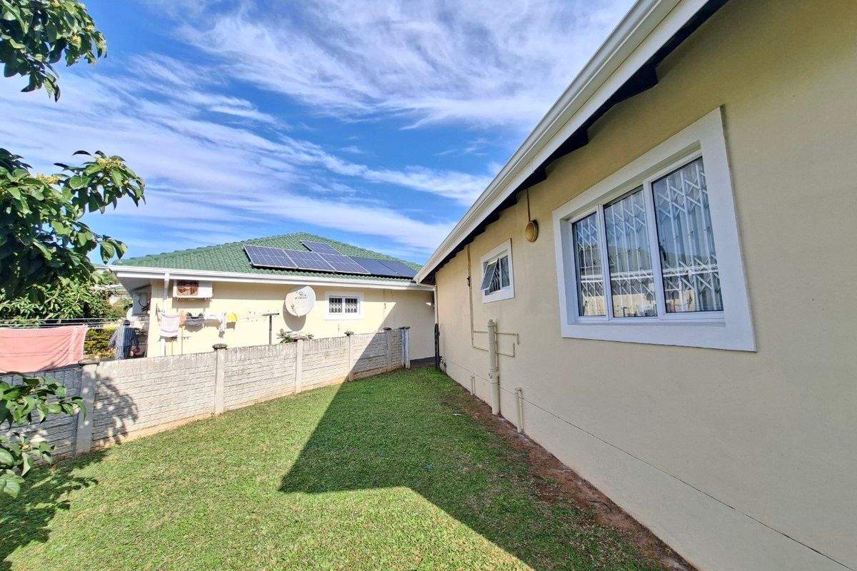A view of the rear exterior of the townhouse, featuring a well-maintained lawn, concrete boundary wall, and secure window installations.