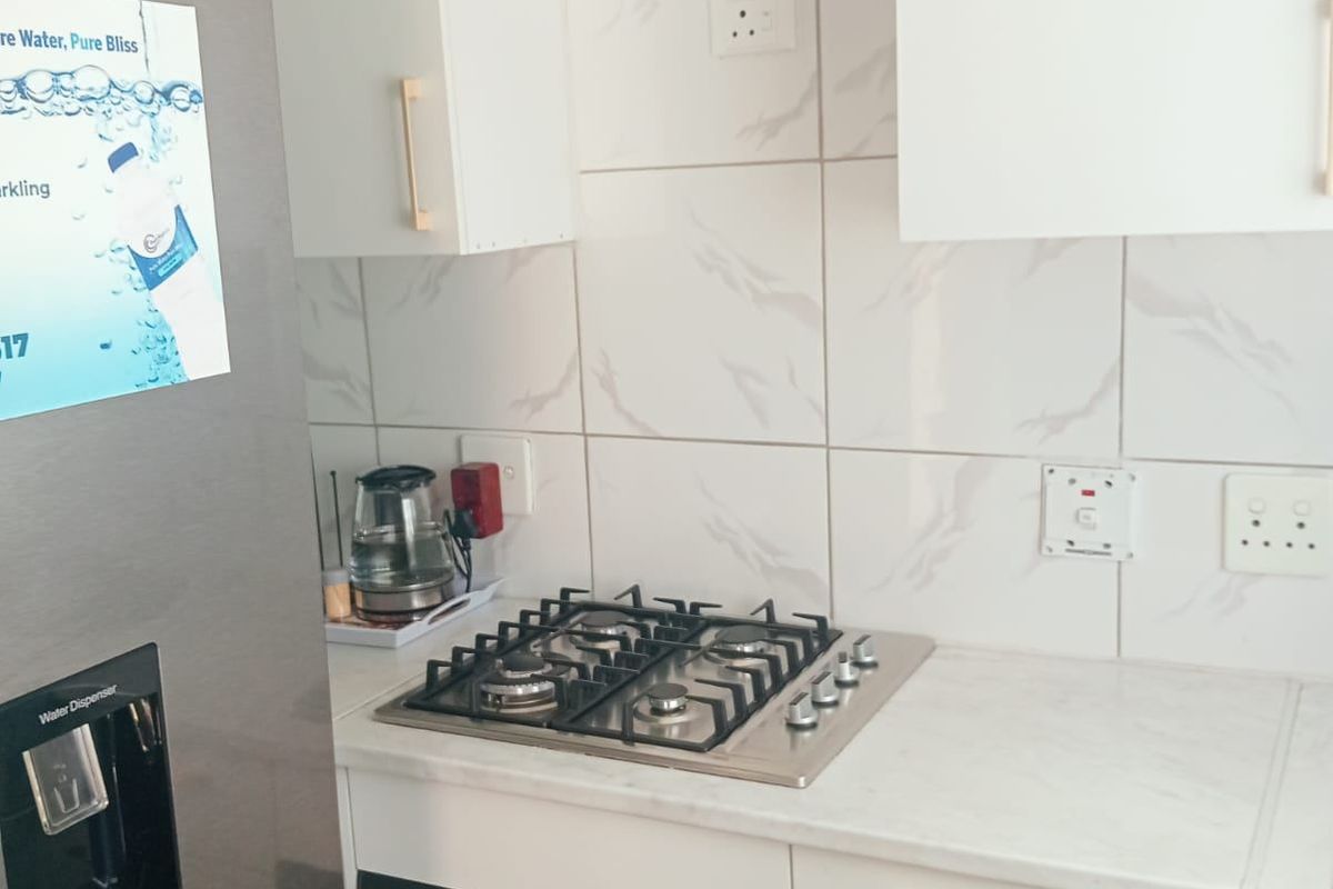 A compact, modern kitchen featuring a built-in oven, gas hob, marble-look countertops, and clean white cabinetry with gold-toned hardware.