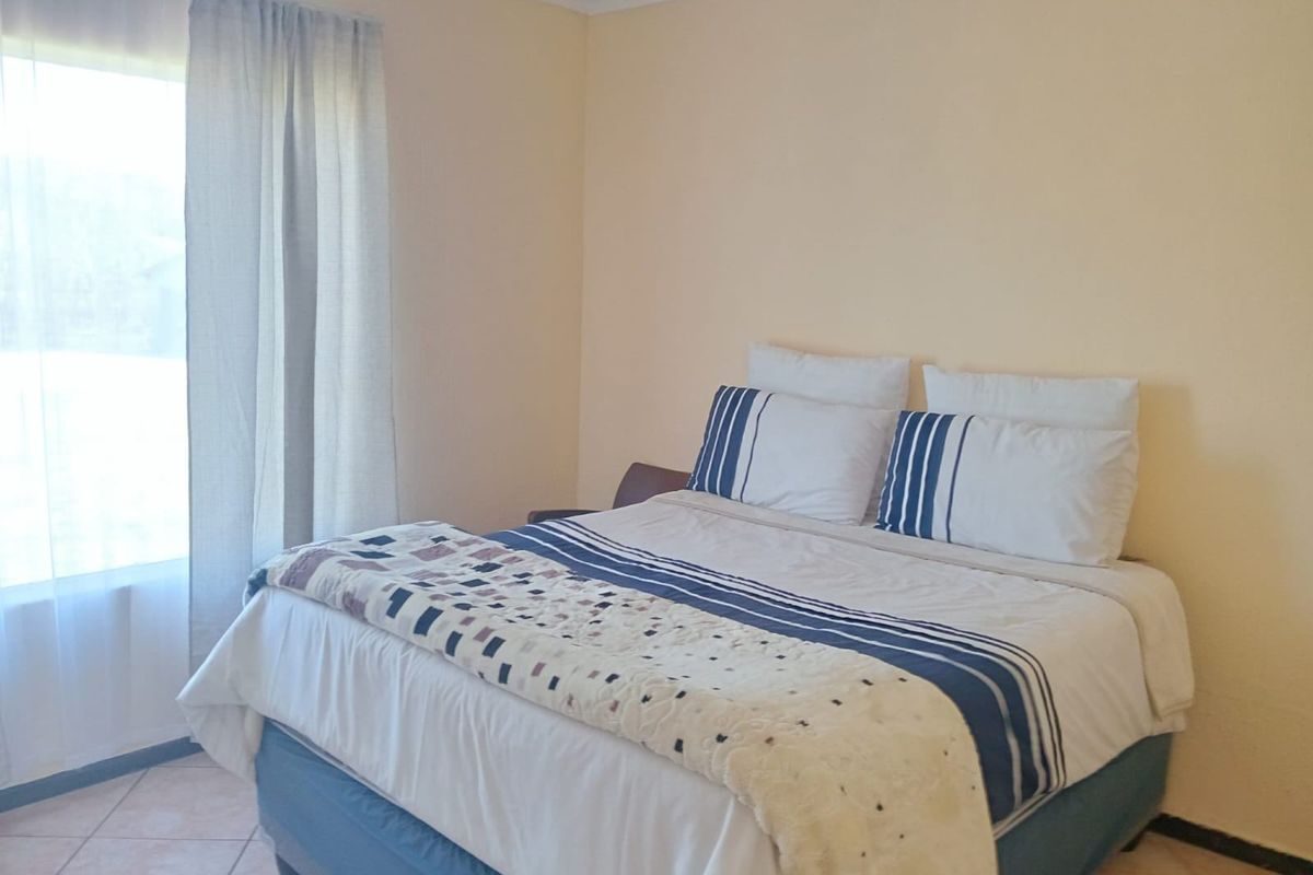 A simple bedroom featuring tiled flooring and natural light from a large window with curtains.