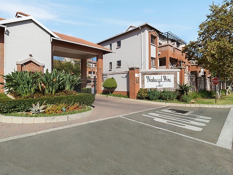 The gated entrance to Westwood Way apartment complex, featuring brick masonry, paved driveway access, and established landscaping.