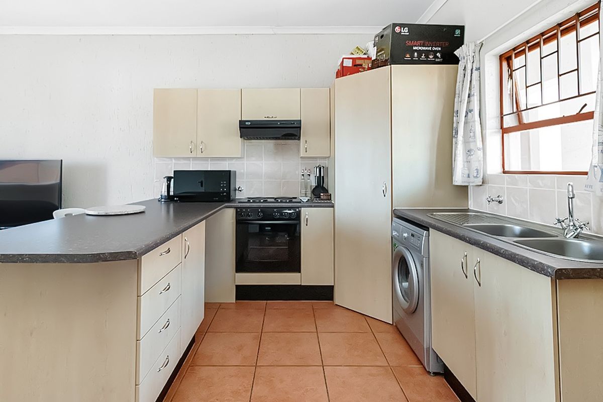 Functional kitchen featuring built-in cabinetry, gas hob, oven, extractor fan, and double bowl sink with tiled splashbacks and ceramic floor tiles.