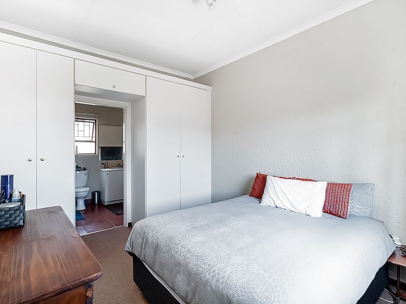 A functional bedroom featuring built-in cupboards and direct access to an en-suite bathroom, offering a practical layout with neutral wall finishes.