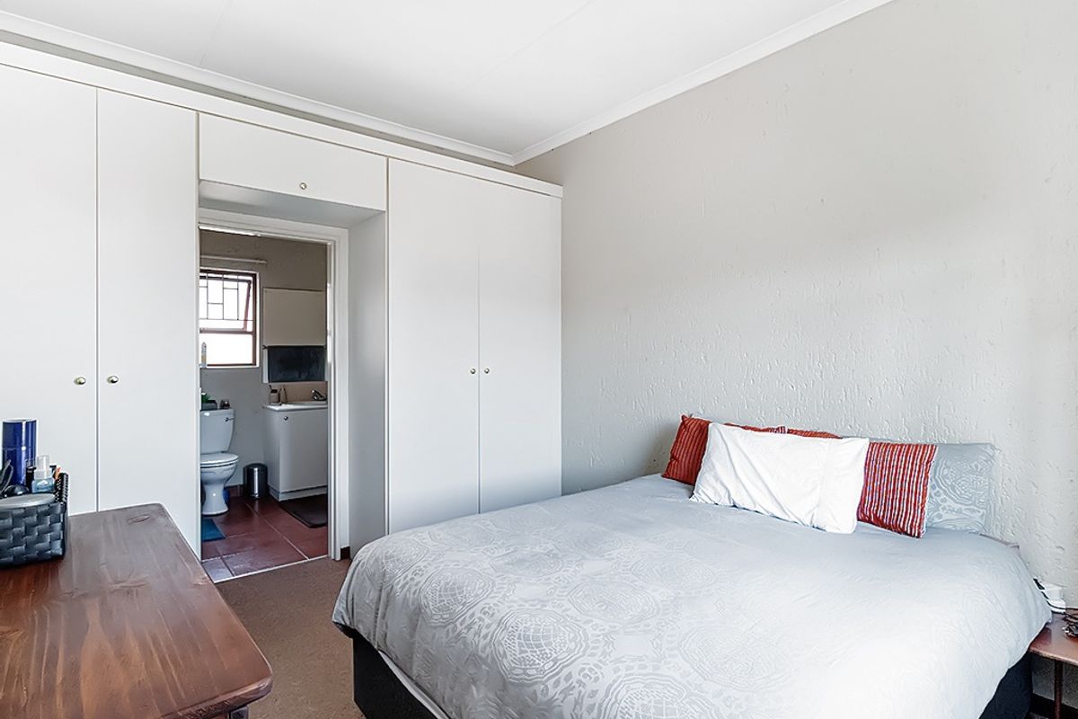 A functional bedroom featuring built-in cupboards and direct access to an en-suite bathroom, offering a practical layout with neutral wall finishes.