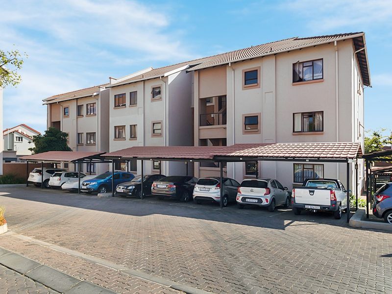 Exterior view of a multi-story apartment complex featuring covered parking bays and a paved driveway area.