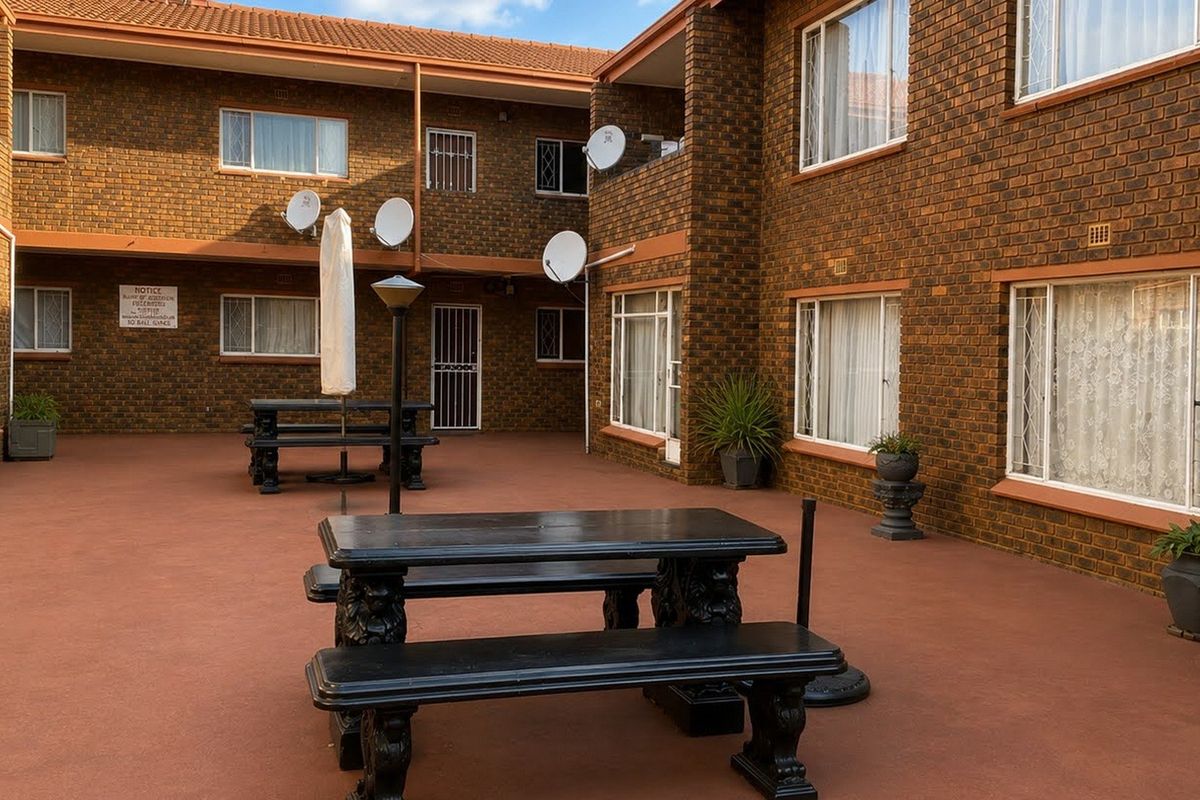 A communal paved courtyard area featuring face brick apartment building facades, security gates, and multiple satellite dish installations.