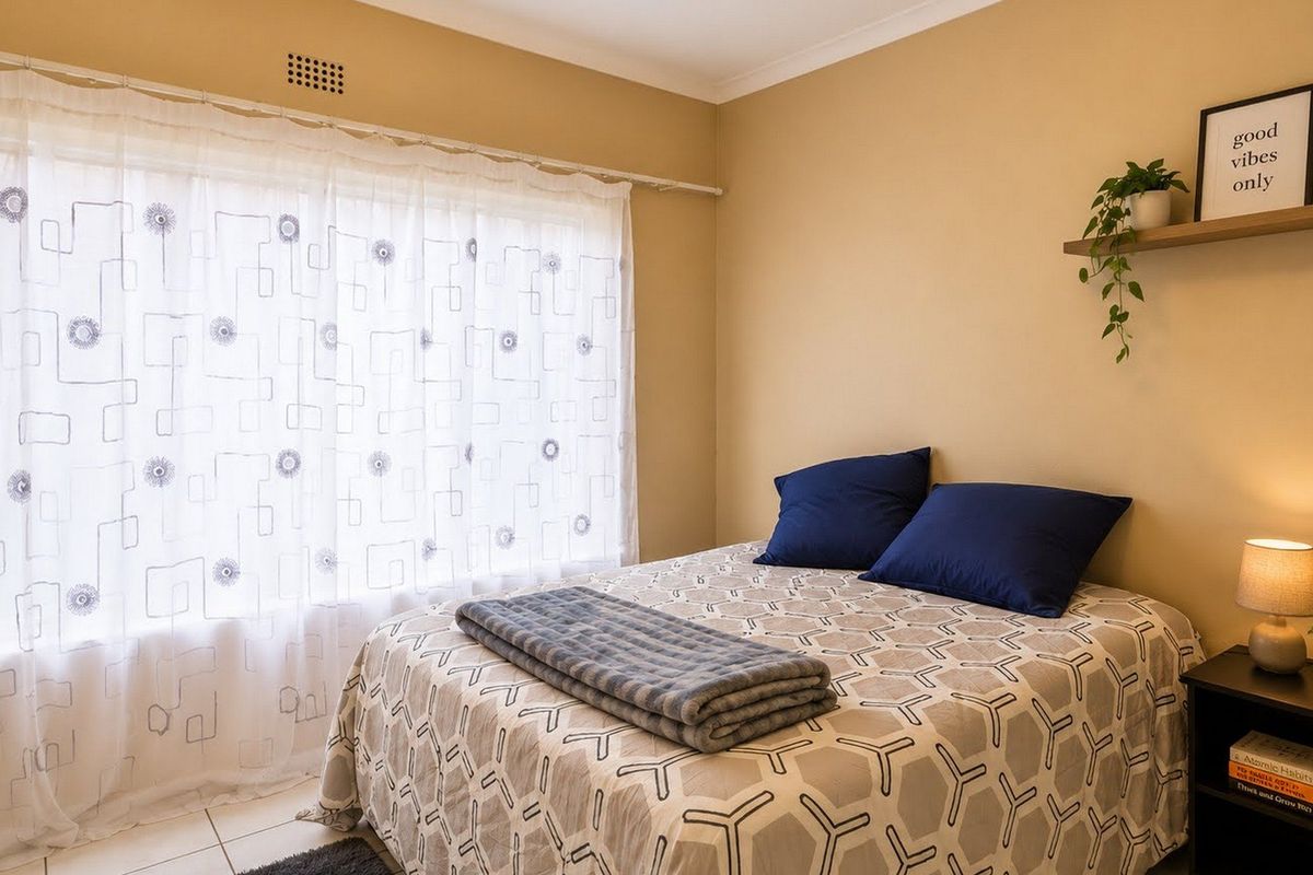 A well-lit bedroom featuring neutral wall tones, tiled flooring, and a large window with sheer curtains.