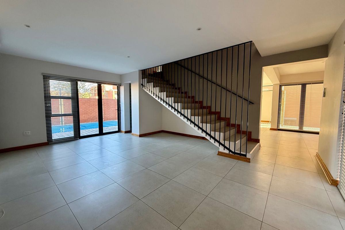 Spacious open-plan living area featuring large format floor tiles, a modern staircase with metal balustrades, and direct access to the outdoor pool area.