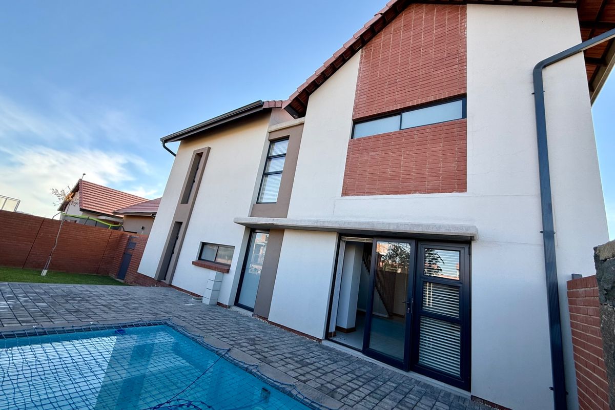 Rear view of the townhouse featuring a paved patio area, swimming pool, and modern architectural facade with brick accents.