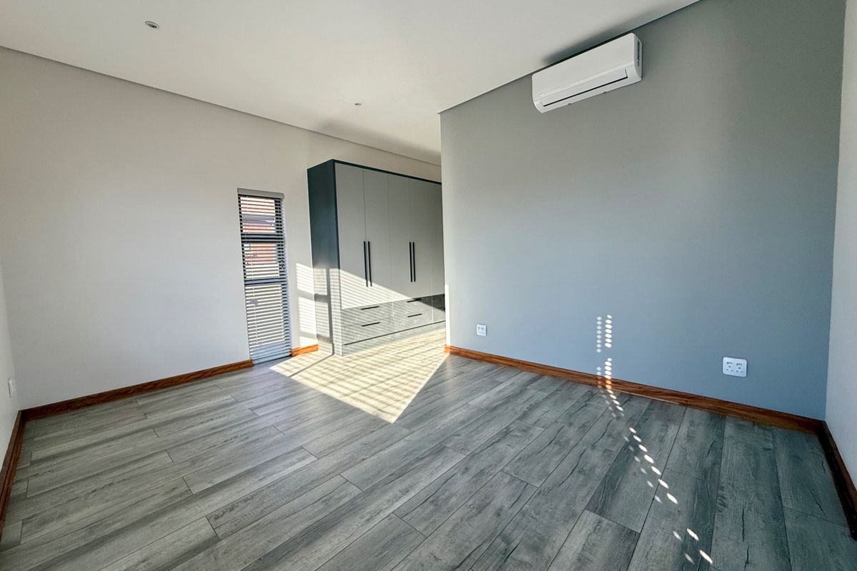 A bright, modern bedroom featuring wood-look laminate flooring, built-in cabinetry, and a wall-mounted air conditioning unit.