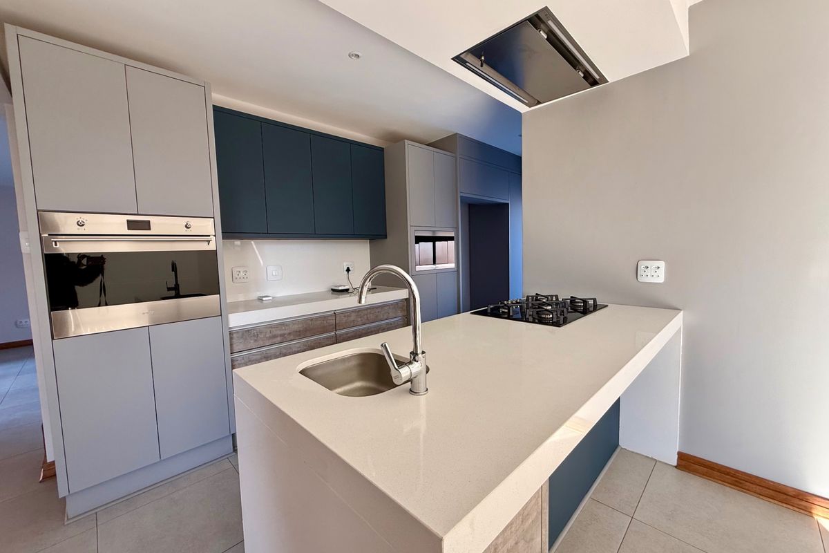 Modern kitchen featuring a central island with a gas hob, undermount sink, built-in oven, and contemporary two-tone cabinetry with quartz countertops.