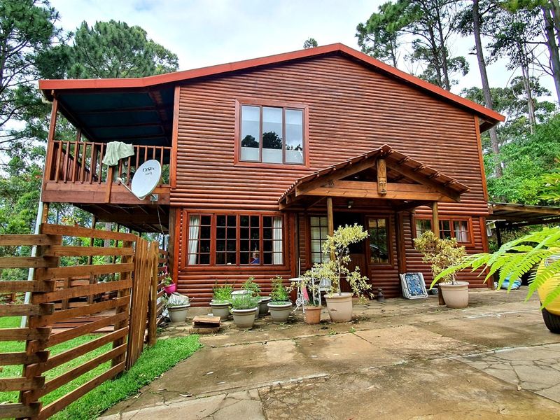 A two-story log cabin style townhouse featuring a timber balcony, covered patio area, and natural wood exterior finishes set in a wooded environment.