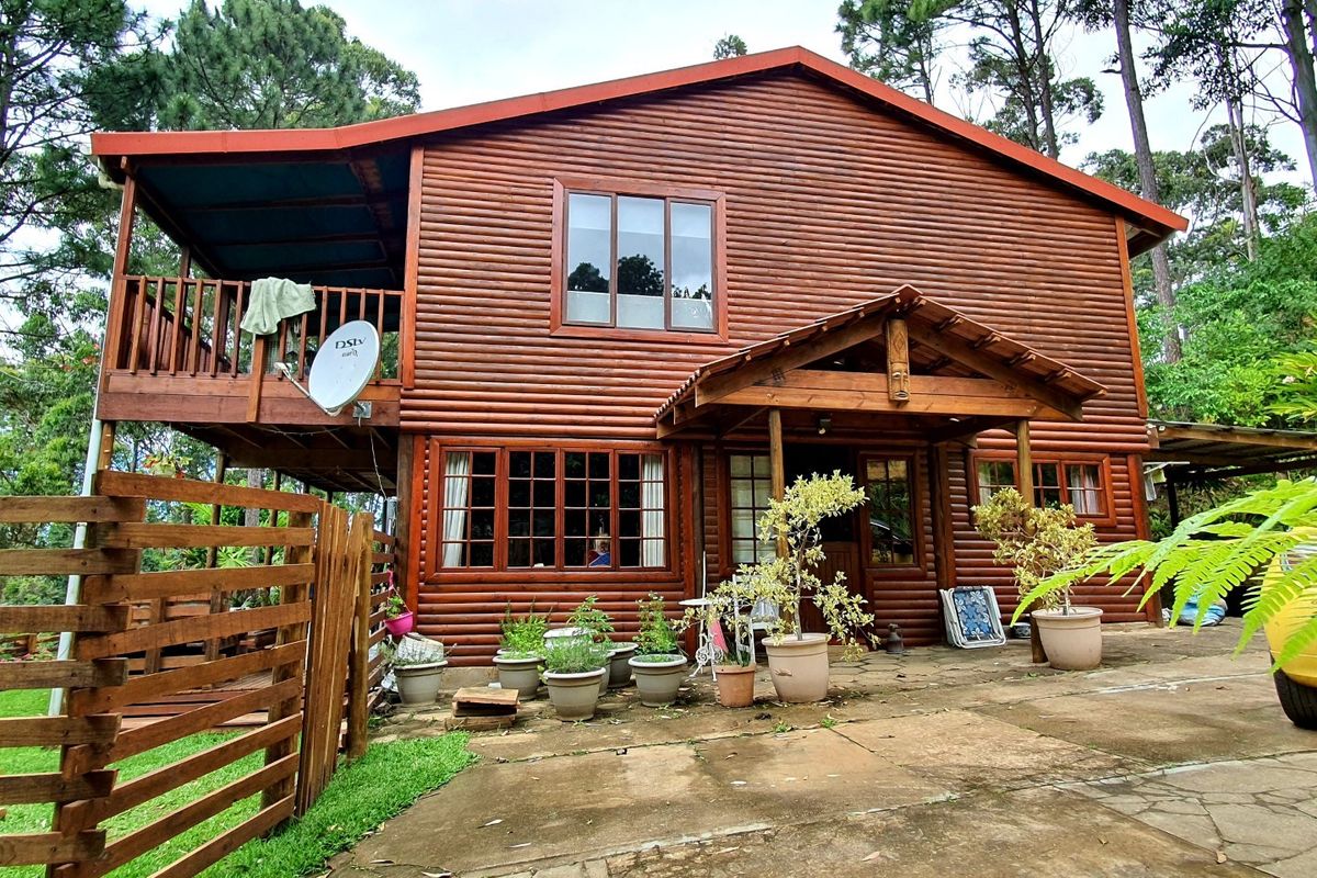 A two-story log cabin style townhouse featuring a timber balcony, covered patio area, and natural wood exterior finishes set in a wooded environment.