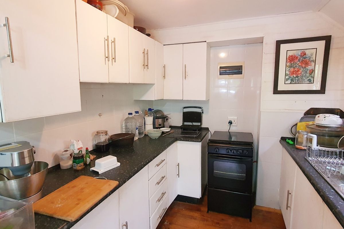 Compact kitchen featuring white cabinetry, dark laminate countertops, tiled backsplash, and a freestanding oven with timber flooring.