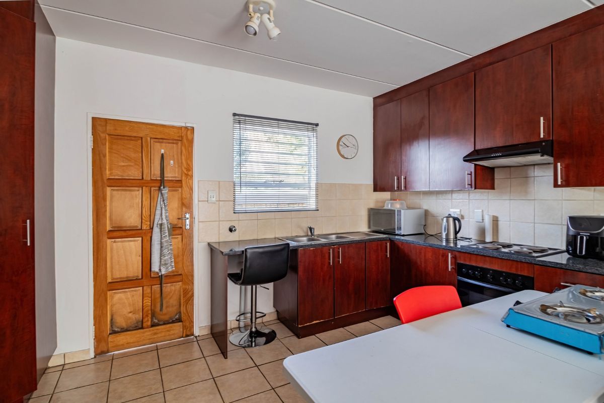 A functional kitchen featuring dark wood cabinetry, tiled backsplash, built-in oven, and hob, with a breakfast nook area and direct access to an exterior door.