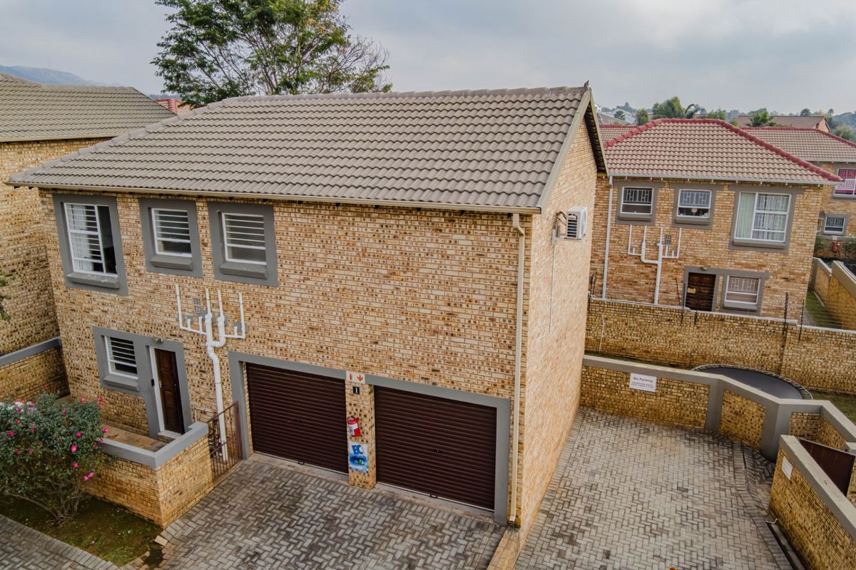 Aerial view of a double-story brick townhouse featuring a double garage, paved driveway, and secure boundary walls within a residential complex.