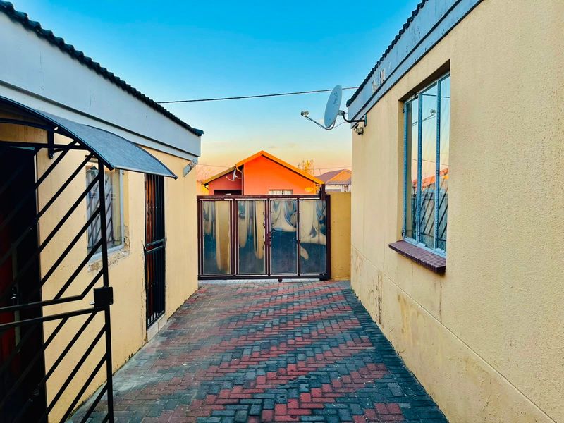 A paved side passage between two residential structures featuring security gates, security bars on windows, and an exterior awning.