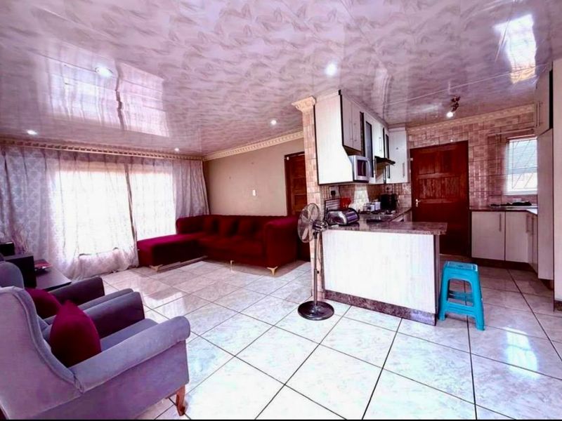 Open-plan living and kitchen area featuring tiled flooring, a kitchen peninsula with built-in cabinetry, and a glossy ceiling finish.