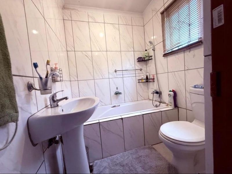 A functional bathroom featuring a pedestal basin, bathtub with shower mixer, and toilet, finished with floor-to-ceiling marble-look wall tiles.