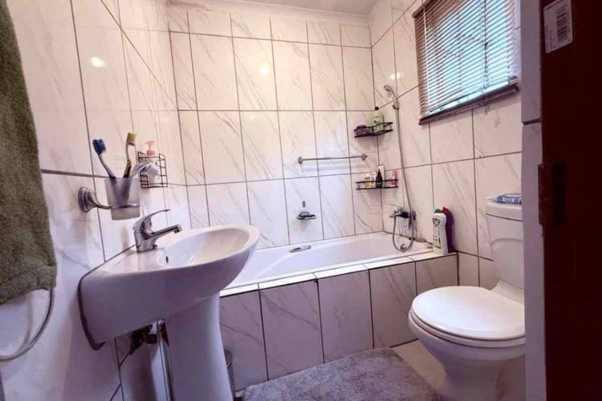 A functional bathroom featuring a pedestal basin, bathtub with shower mixer, and toilet, finished with floor-to-ceiling marble-look wall tiles.