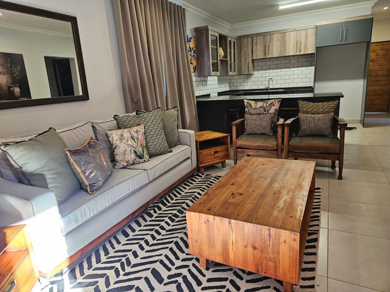 Open-plan living area featuring a modern kitchen with dark cabinetry, subway tile backsplash, and a breakfast island, seamlessly connected to the lounge space.
