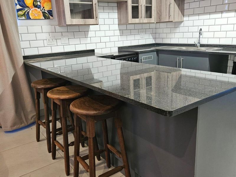 Modern kitchen featuring granite countertops, a breakfast bar, subway tile backsplash, and ample built-in cabinetry with a neutral color palette.
