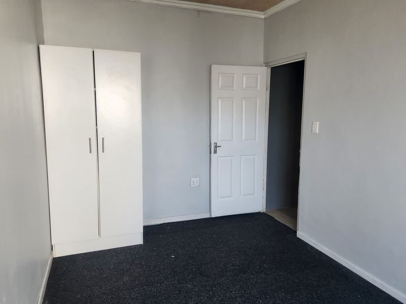 A simple bedroom featuring grey walls, dark carpeting, and a built-in wardrobe, offering a blank canvas for potential updates.