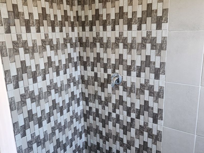 A shower enclosure featuring patterned wall tiling, a wall-mounted electric shower head, and a chrome mixer tap.