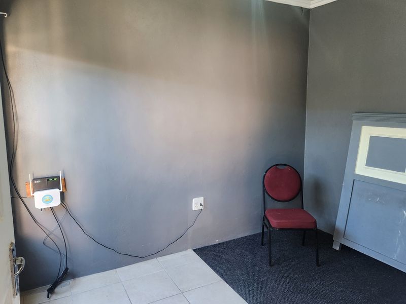 A sparsely furnished room featuring a mix of tiled and carpeted flooring with grey painted walls and visible electrical infrastructure.