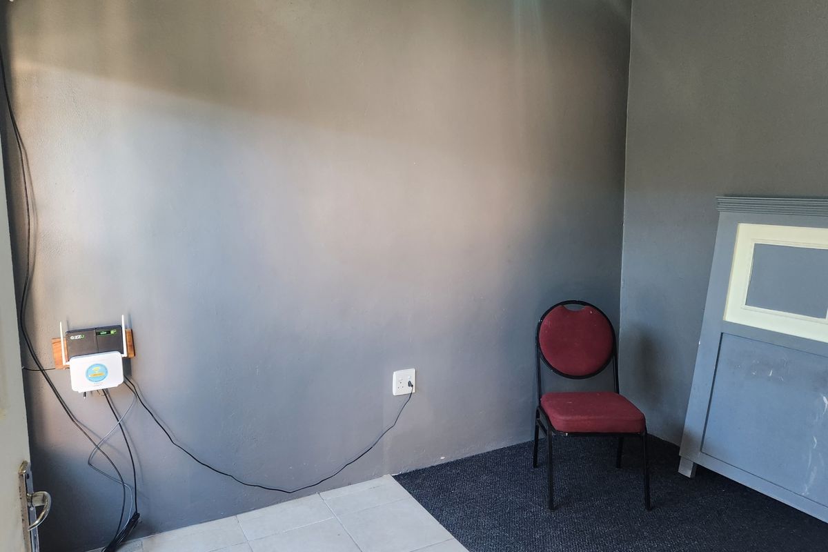 A sparsely furnished room featuring a mix of tiled and carpeted flooring with grey painted walls and visible electrical infrastructure.
